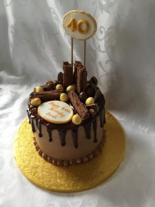 A chocolate birthday cake covered with chocolate buttercream, with dark chocolate ganache drip coat, decorated with a personal dedication and chocolate treats.